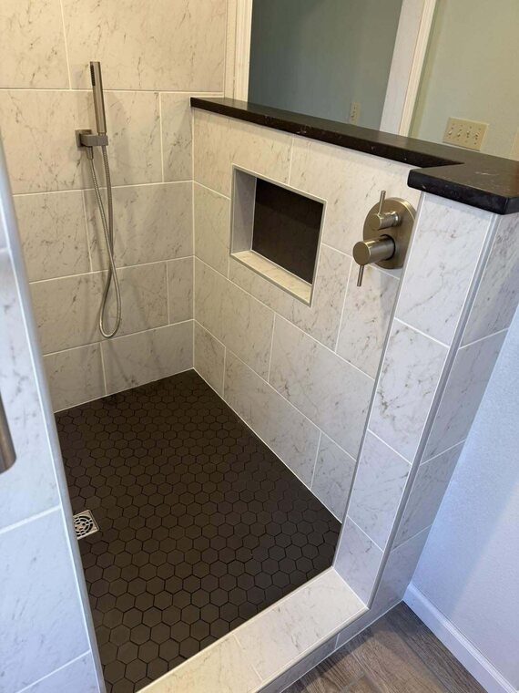 Walk in shower with white marble look tile, dark hexagon floor tile, recessed niche, and handheld sprayer
