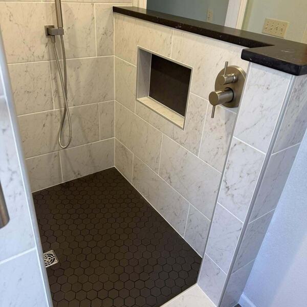 Walk in shower with white marble look tile, dark hexagon floor tile, recessed niche, and handheld sprayer
