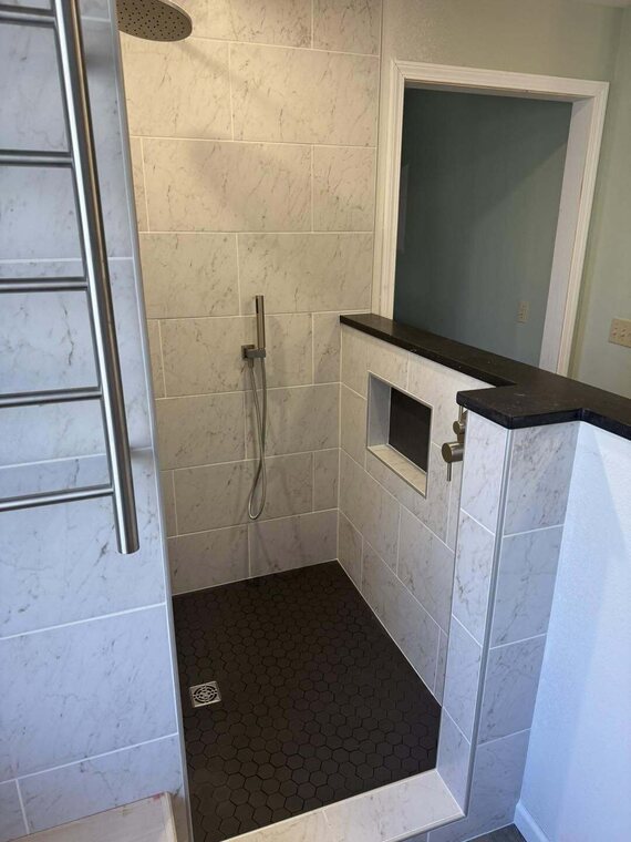 Walk in tiled shower with light marble look wall tile, black hexagon floor tile, rainfall head, and niche
