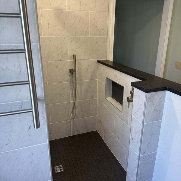 Walk in tiled shower with light marble look wall tile, black hexagon floor tile, rainfall head, and niche