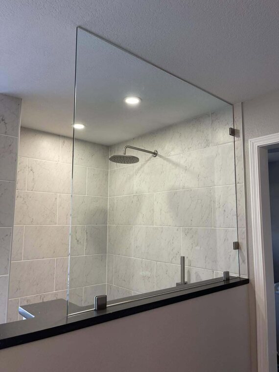 Walk in shower with marble look tile, rain shower head, and a glass partition panel