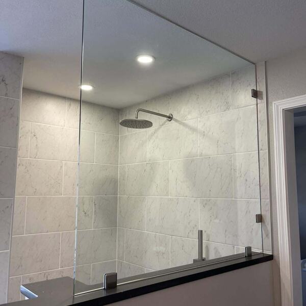 Walk in shower with marble look tile, rain shower head, and a glass partition panel
