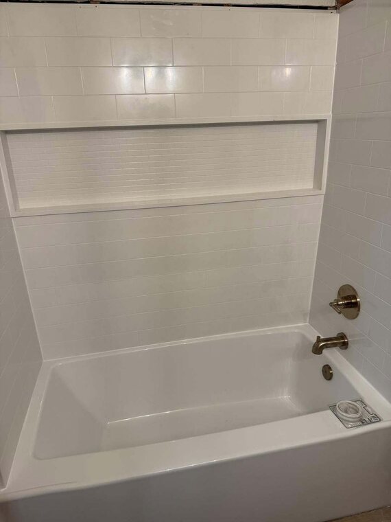White tiled tub surround with recessed niche and gold tone tub spout and handle