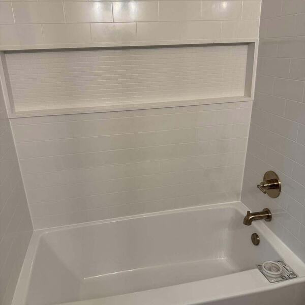 White tiled tub surround with recessed niche and gold tone tub spout and handle