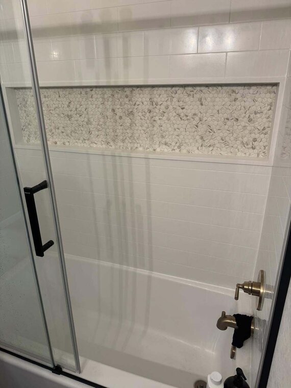 Tiled tub and shower surround with penny tile accent niche, glass door, and brushed gold tub fixtures