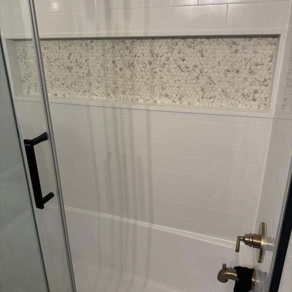 Tiled tub and shower surround with penny tile accent niche, glass door, and brushed gold tub fixtures