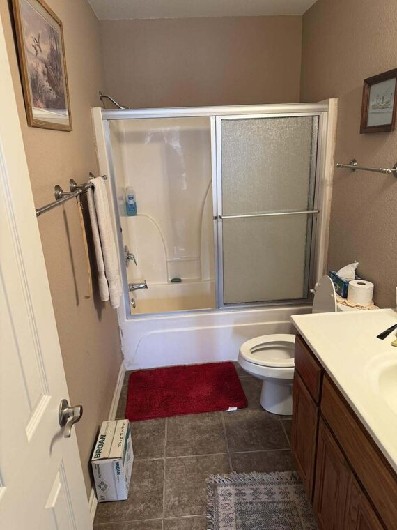 Dated bathroom with tub and sliding glass shower doors toilet wood vanity and tile floor