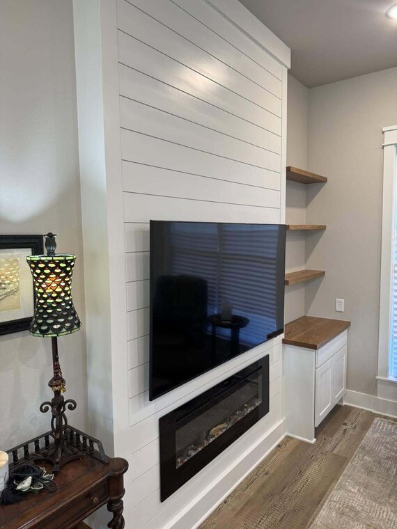White shiplap fireplace wall with mounted TV electric fireplace floating wood shelves and white cabinet