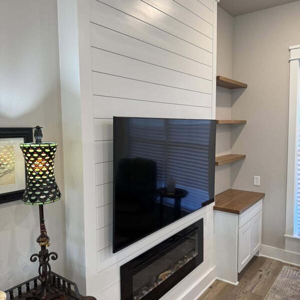 White shiplap fireplace wall with mounted TV electric fireplace floating wood shelves and white cabinet