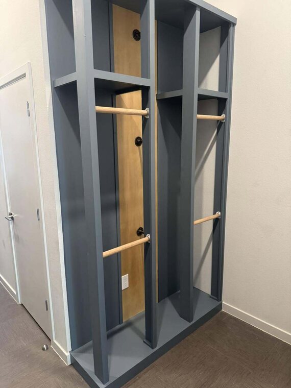 Custom blue gray built in locker unit with wood hanging rods against a wall near a door