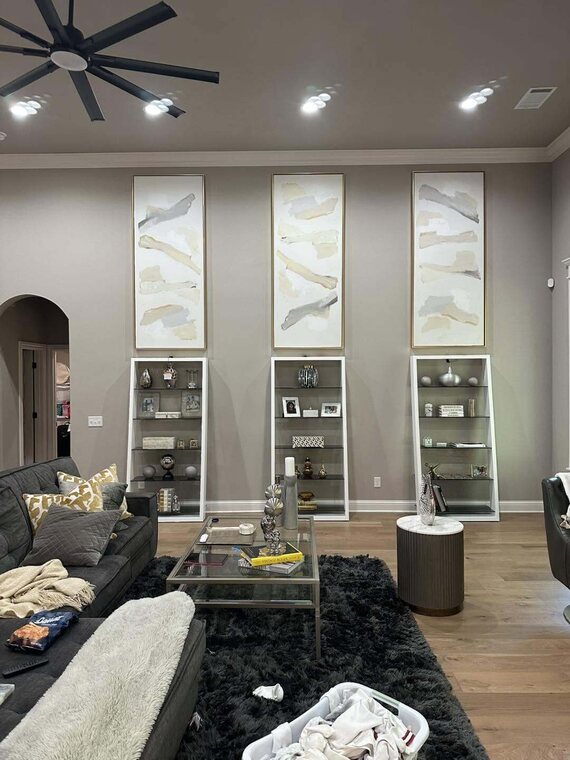 Living room with three tall white built in display shelves and large black ceiling fan
