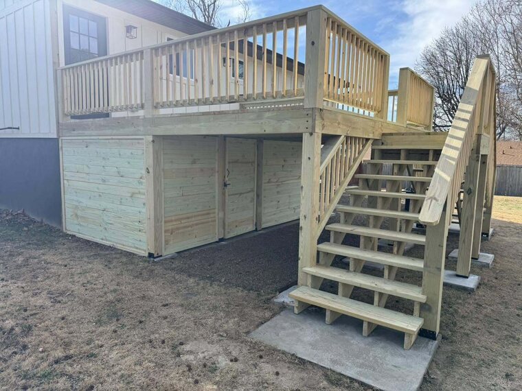 Raised wood deck with railing, staircase and enclosed storage area underneath beside a home