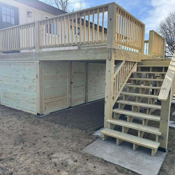 Raised wood deck with railing, staircase and enclosed storage area underneath beside a home
