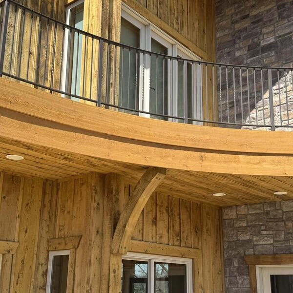 Curved wood balcony and covered porch ceiling with metal railing over stone and wood siding