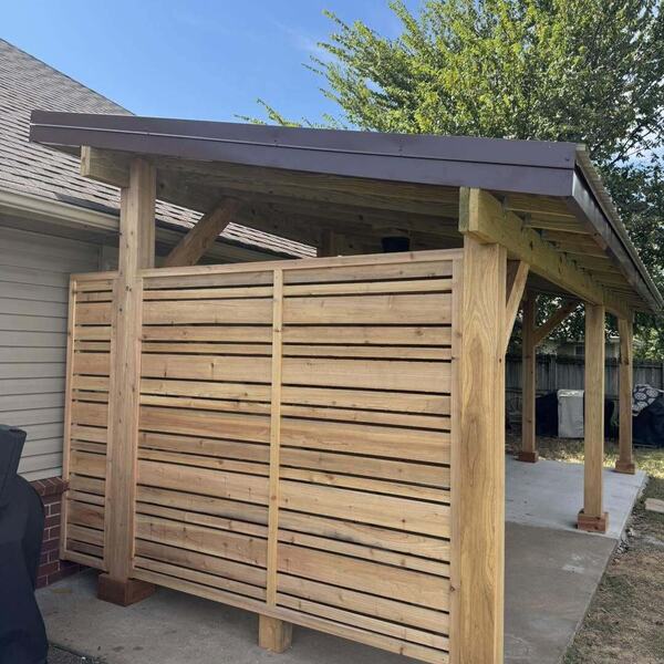 Wood patio cover with slatted privacy wall over a concrete pad beside a house