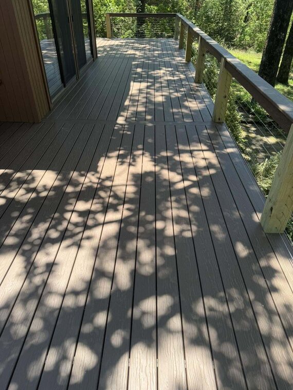 Composite deck boards with wood frame cable railing beside a home with sliding glass doors and trees