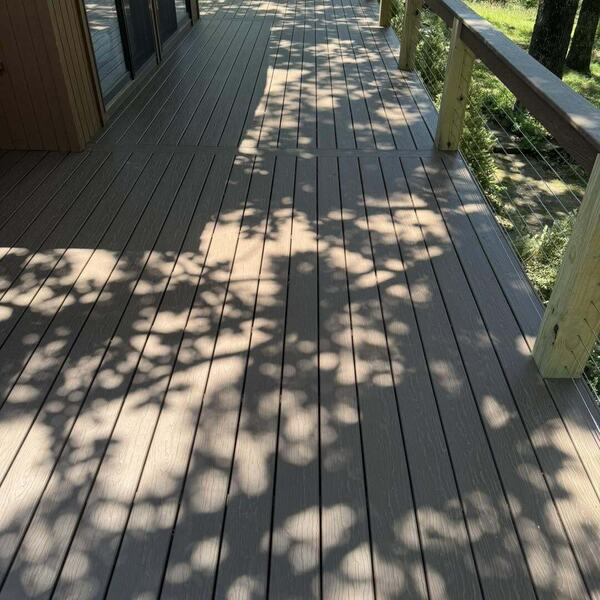 Composite deck boards with wood frame cable railing beside a home with sliding glass doors and trees