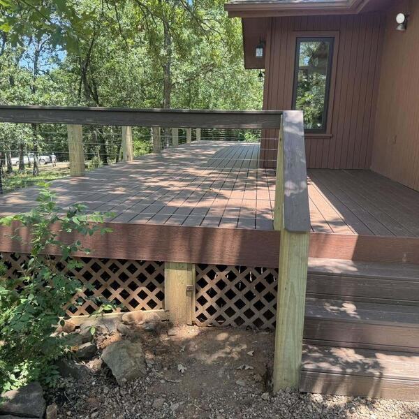 Wood deck with cable railing and lattice skirting beside a wood sided home in a wooded yard