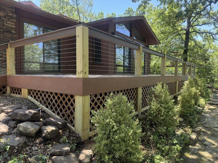 Raised wood deck with cable railing and lattice skirting along the side of a wood and stone home