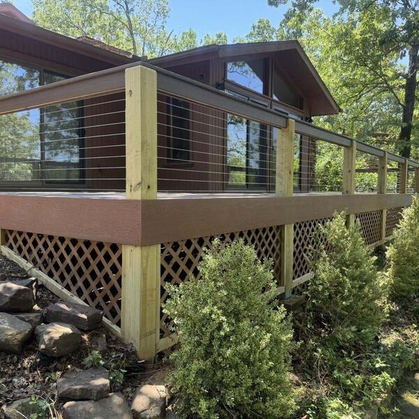 Raised wood deck with cable railing and lattice skirting along the side of a wood and stone home