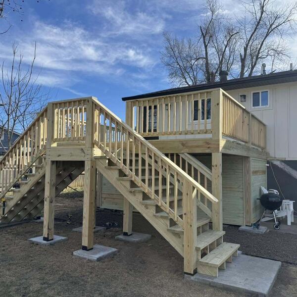 Newly built raised wood deck with two staircases on the back of a two story house