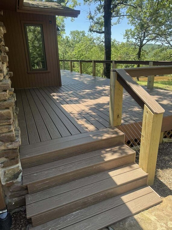 Finished composite deck with steps and a wood post cable railing overlooking wooded hills