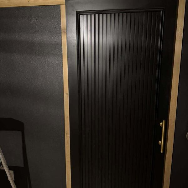 Black sliding barn door with vertical grooved panel and brass bar pull on black hardware over light wood floor