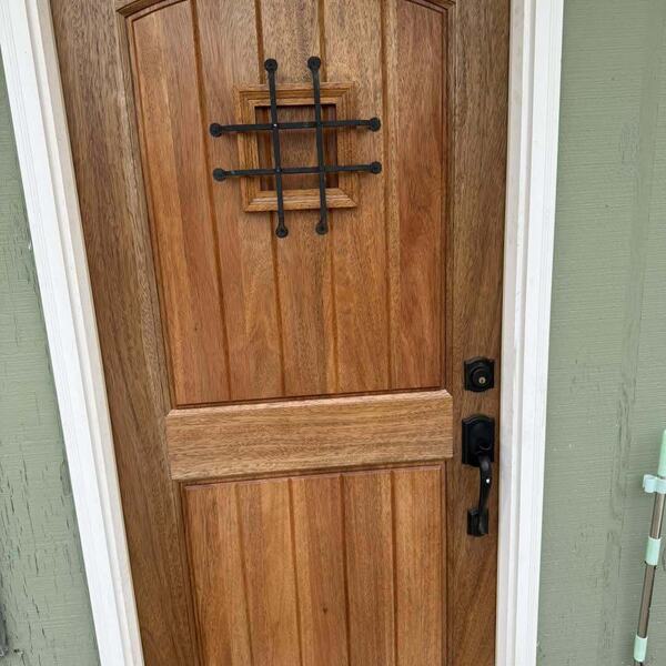 Stained wood exterior entry door with iron speakeasy grille and dark handleset on green wall