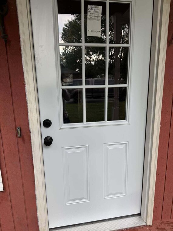 New white exterior door with nine pane window grid installed in red sided wall