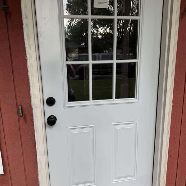 New white exterior door with nine pane window grid installed in red sided wall