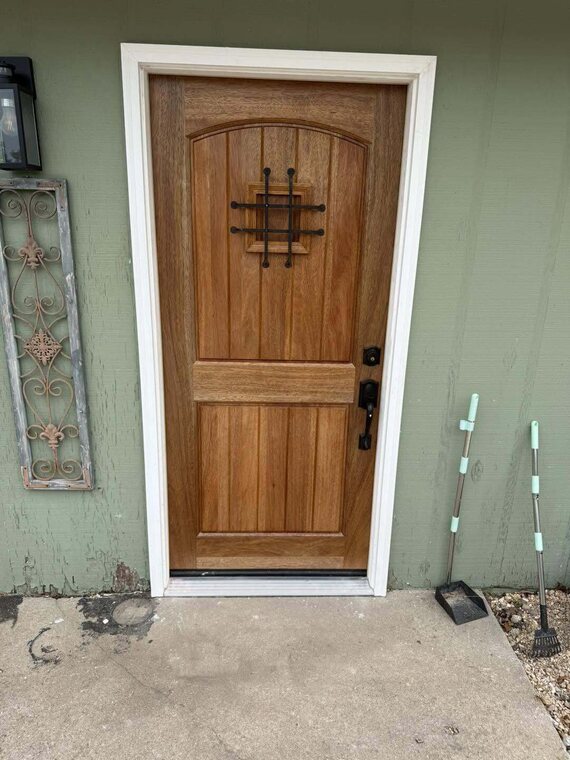Wood stained exterior door with speakeasy grille set in green sided wall