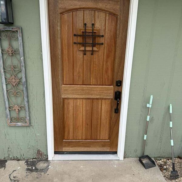 Wood stained exterior door with speakeasy grille set in green sided wall