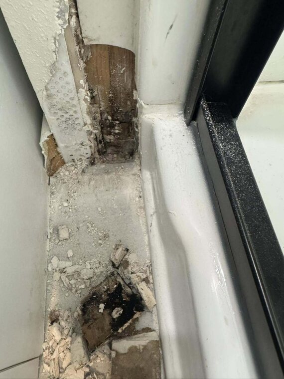 Close up of a sliding door threshold and jamb showing rotted wood, crumbling material, and water damage