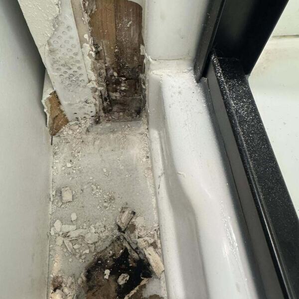 Close up of a sliding door threshold and jamb showing rotted wood, crumbling material, and water damage