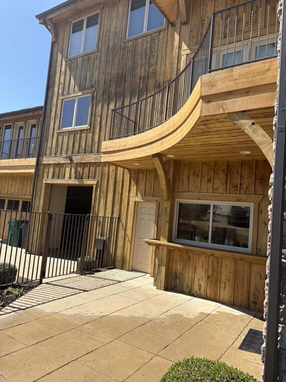 Multi story building with vertical wood plank siding, a curved wood balcony, metal railings and a stamped concrete patio