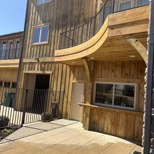 Multi story building with vertical wood plank siding, a curved wood balcony, metal railings and a stamped concrete patio