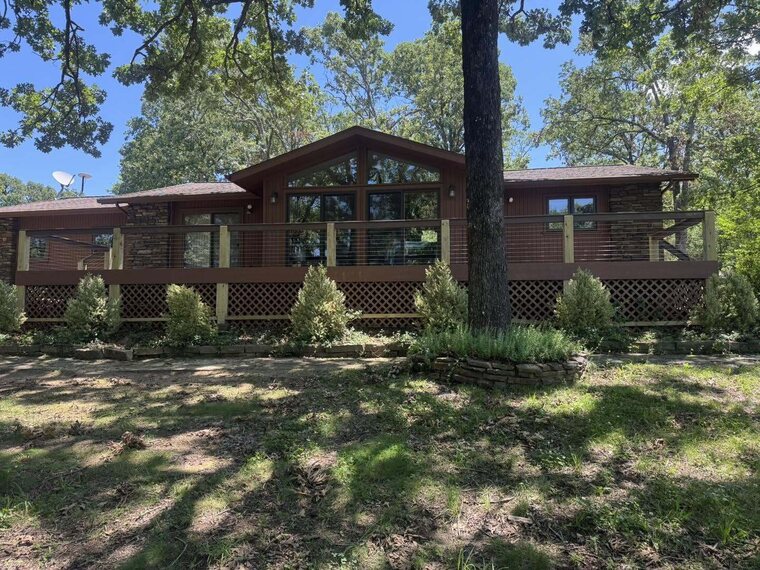 Single story dark wood sided home with a porch and large windows surrounded by trees