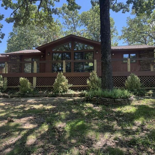 Single story dark wood sided home with a porch and large windows surrounded by trees
