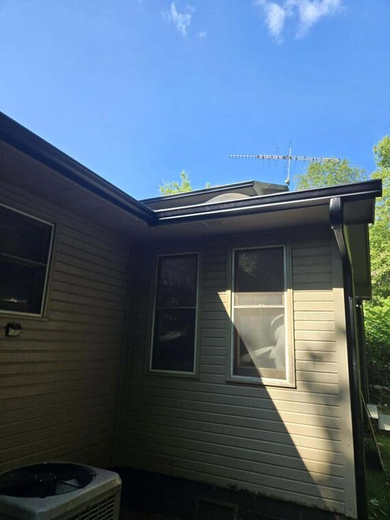 Corner of a home with lap siding, windows, and dark fascia trim and a dark downspout under a blue sky
