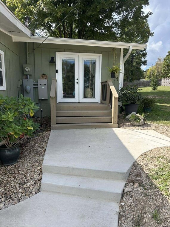 Concrete walkway and steps leading to a French door entry on a green sided house
