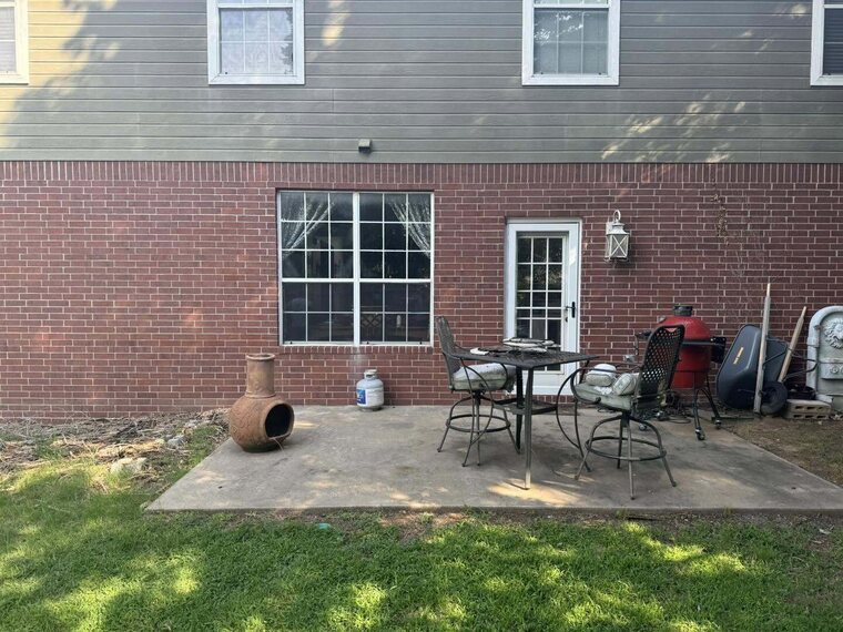 Back of a brick two story home with a concrete patio holding a table chairs and a chiminea