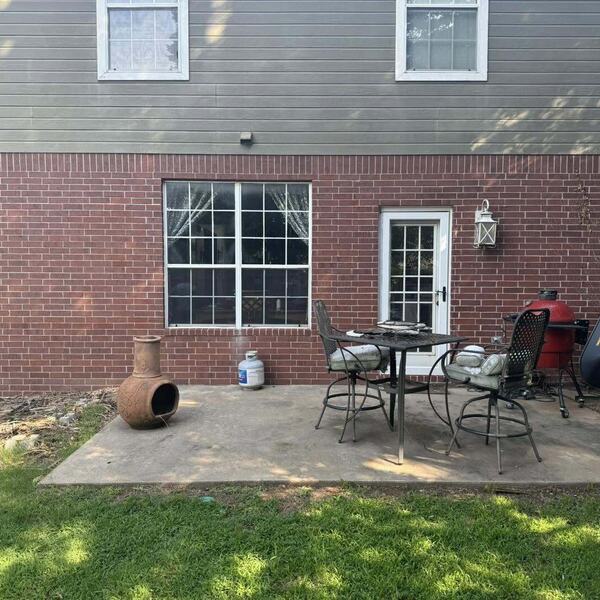 Back of a brick two story home with a concrete patio holding a table chairs and a chiminea