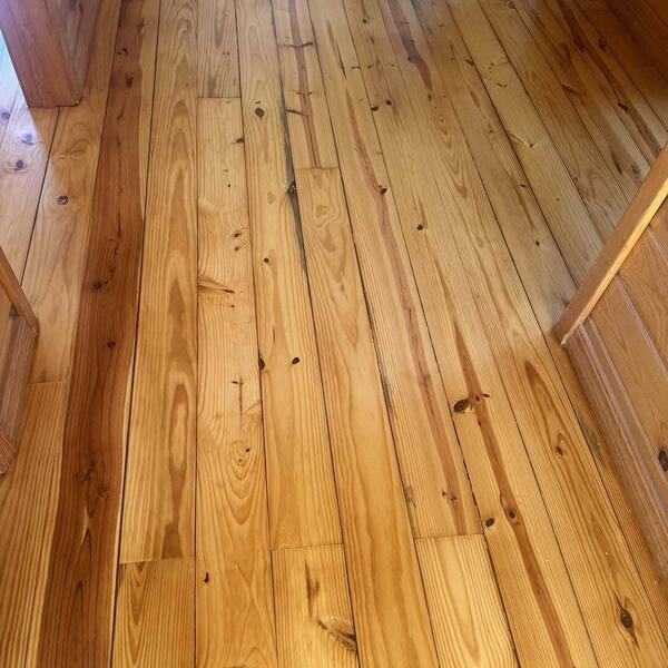 Refinished pine plank flooring with visible wood grain between wood cabinetry