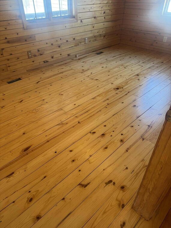 Room with knotty pine wood plank floor and matching pine plank walls with two window openings