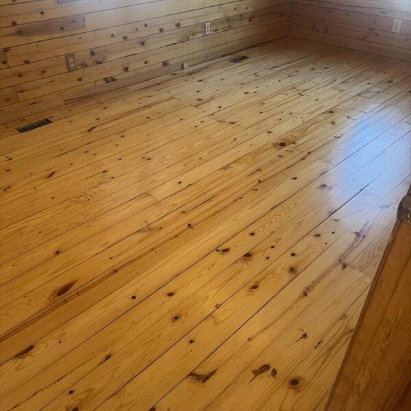 Room with knotty pine wood plank floor and matching pine plank walls with two window openings