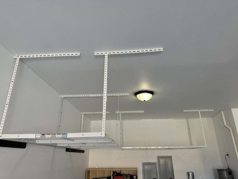 White overhead ceiling mounted storage rack installed in a garage near a dome ceiling light