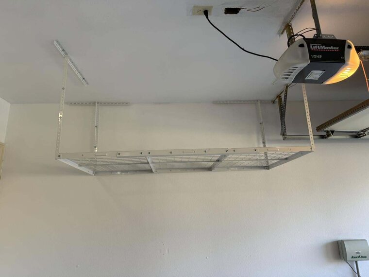 Overhead wire storage rack mounted to a garage ceiling near a garage door opener