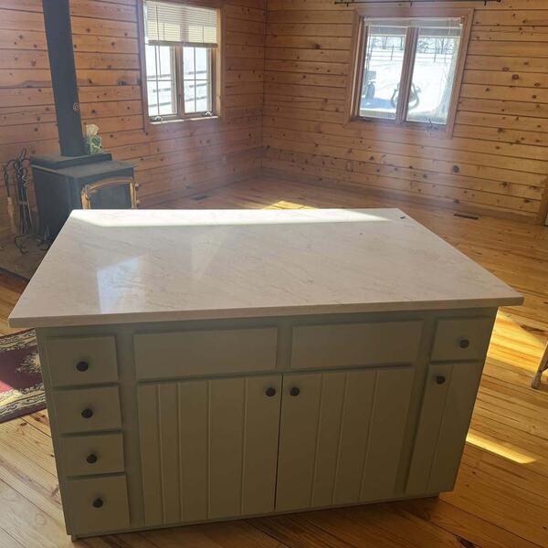 Kitchen island with sage green cabinets and a light stone top in a wood paneled room with a wood stove