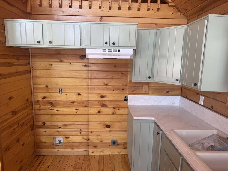 Cabin kitchen with green cabinets, white range hood, light countertop and double sink against knotty pine walls