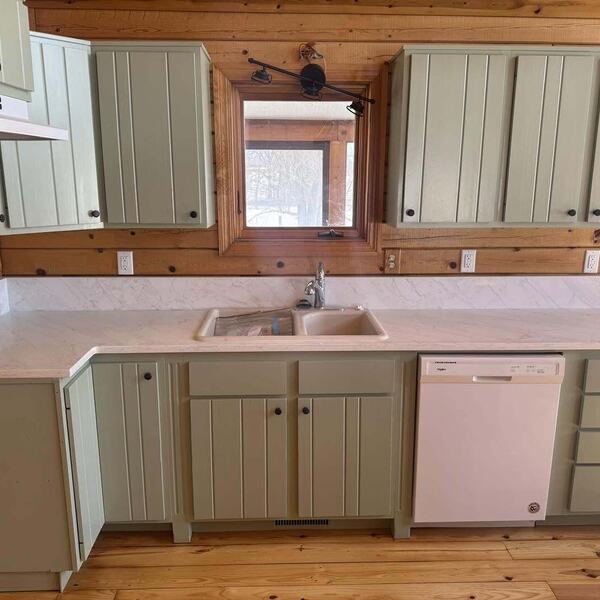 Kitchen with sage green cabinets, light veined countertop, white dishwasher, beige sink and wood plank floor